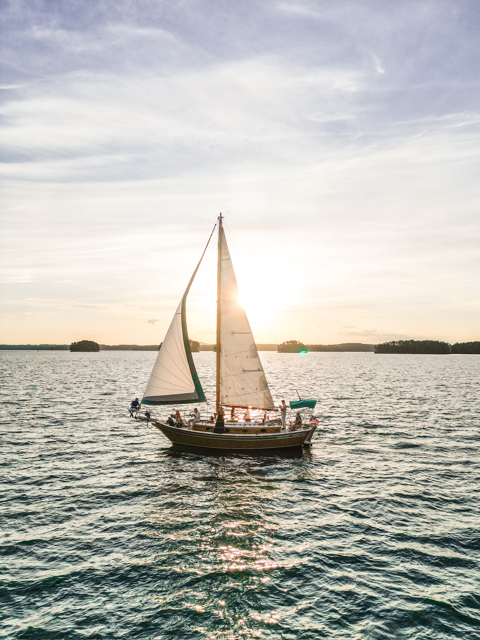 Aerial view of a sailboat gliding across Lake Lanier at sunset with golden light reflecting off the water